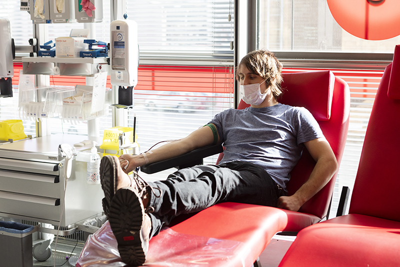 Verenluovuttaja Sanomatalon toimipisteellä, istuu verenluovutuspdeillä ja aurinko paistaa.