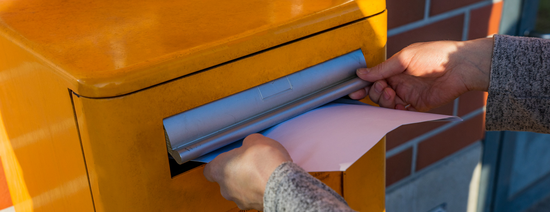 Hands push a letter into Posti's mailbox.