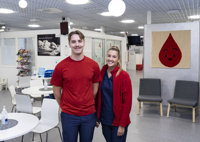 Kaksi Veripalvelun hoitajaa hymyilee kameralle verenluovutuspisteessä.