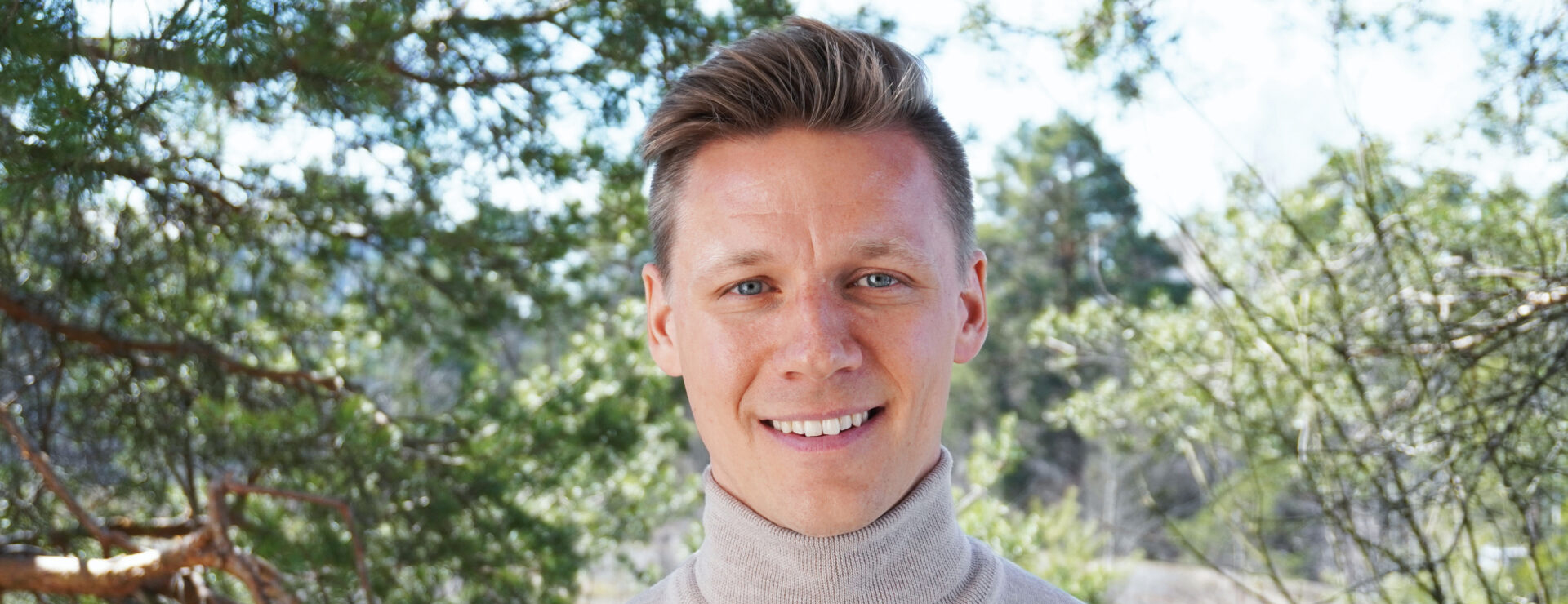 The blond-haired man looks at the camera and smiles.