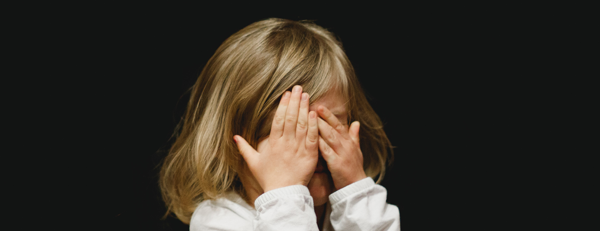 A little girl with her hands over her eyes.