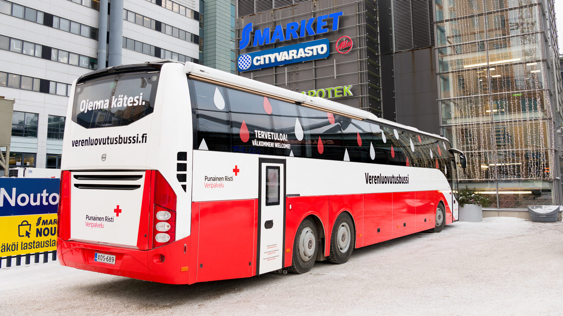Punavalkoinen Verenluovutusbussi ostoskeskuksen pihalla.