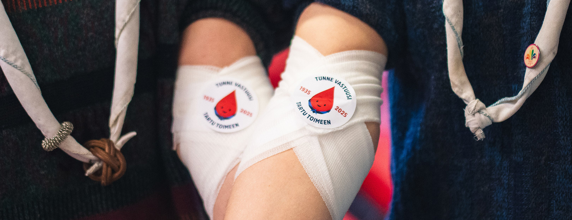 Kahden verenluovuttajan kädet vierekkäin. Kyynärtaipeissa sideharsot, joissa partiolaisten verenluovutuskampanjan tarrat.