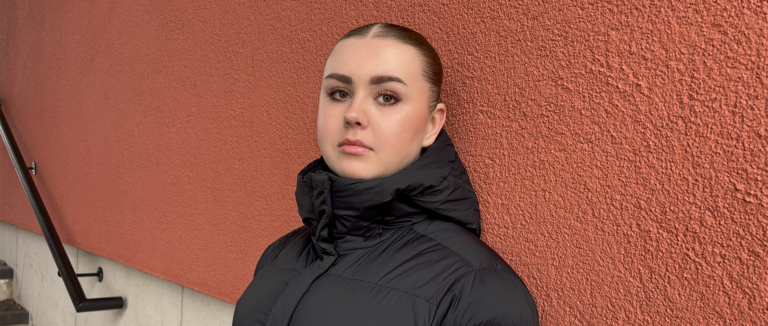 Nuppu Toivonen kuvattuna ulkona, nojaa seinään ja katsoo kameraan.