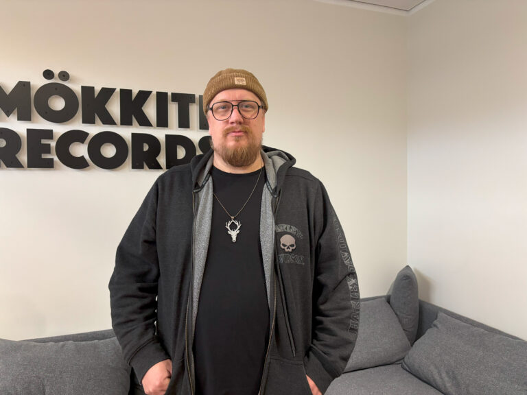 Muusikko Arttu Wiskari katsoo kameraan. Hänen takanaan näkyy Mökkitie Recordsin teksti.