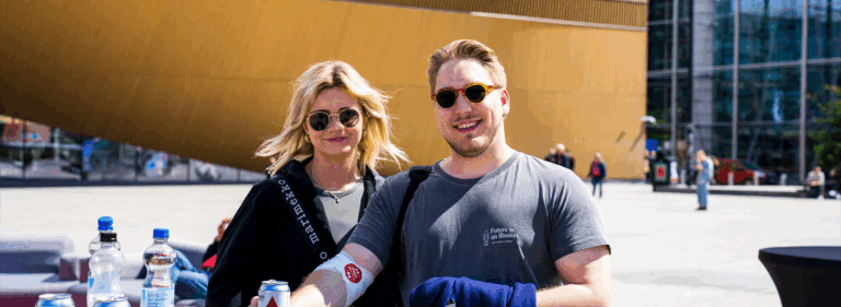 Kaksi hymyilevää henkilöä kuvattuna ulkona Veripalvelun kesätapahtumassa Maailman verenluovuttajien päivänä.