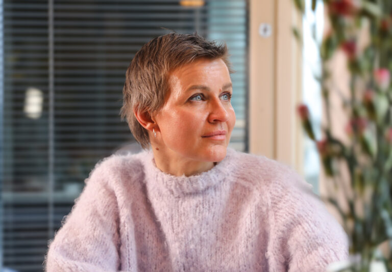 Milla Madetoja istuu pöydän äärellä ja katsoo ikkunasta ulos.